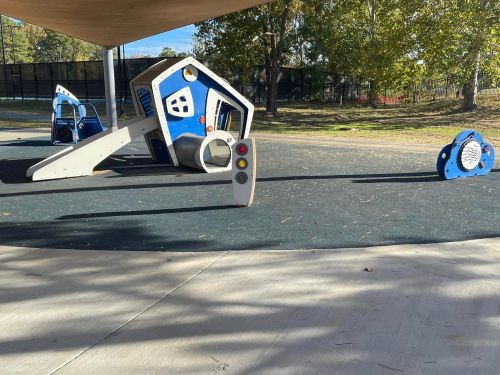Playground equipment featuring a blue and white climbing structure and a small play panel, set in a grassy area.