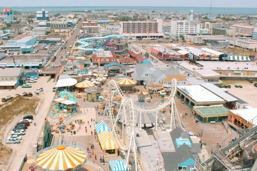 Aerial view of a bustling amusement park with rides, colorful tents, and nearby buildings along the coast.