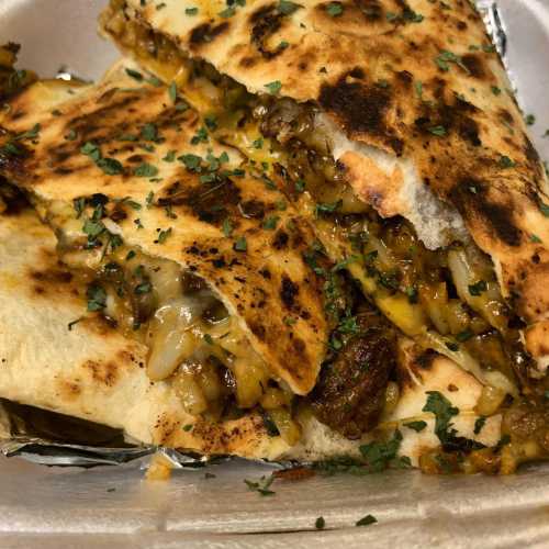 A close-up of a grilled quesadilla filled with melted cheese, meat, and herbs, served on a white plate.