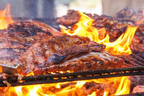 Grilled meat sizzling over flames, showcasing juicy ribs with a smoky char on a barbecue grill.