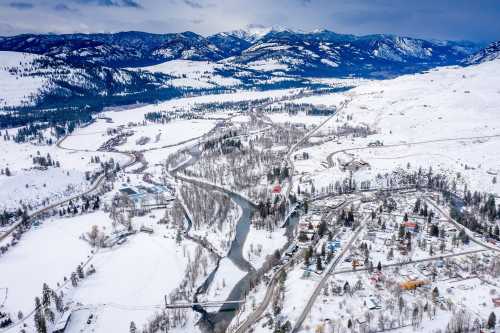 Aerial view of a snowy landscape with a winding river, mountains, and a small town nestled in the valley.