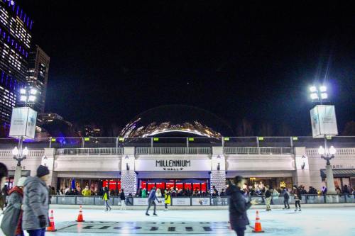 A bustling ice skating rink at night, with the Millennium Park pavilion illuminated and people skating.