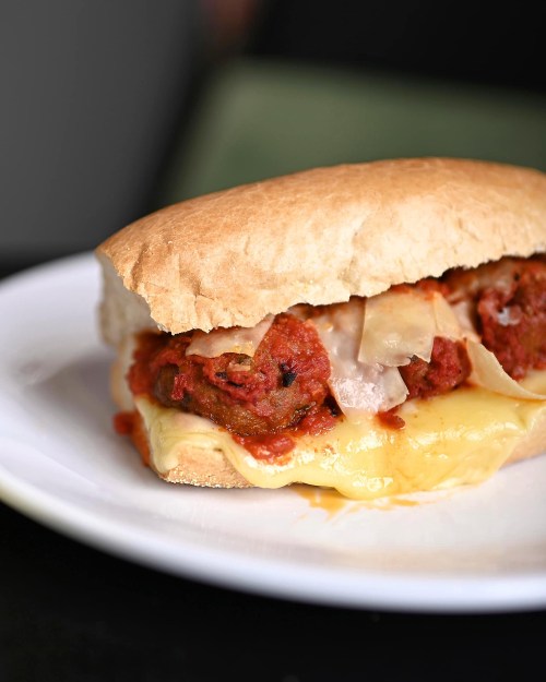 A hearty meatball sandwich with marinara sauce and melted cheese on a soft roll, served on a white plate.