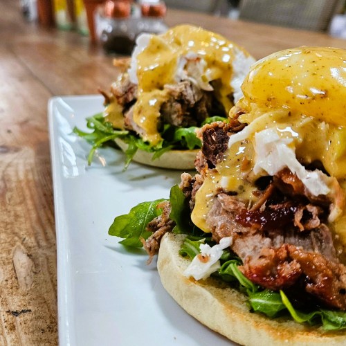 A plate of pulled pork on a bun, topped with mustard sauce and served on a bed of greens.