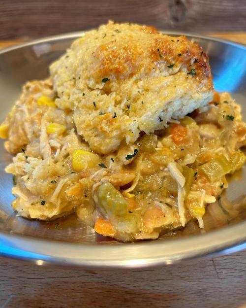 A bowl of creamy chicken and vegetable casserole topped with a golden biscuit.