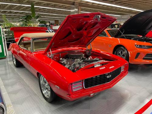 A red 1969 Chevrolet Camaro SS with the hood open, showcasing its engine, parked in a car show.