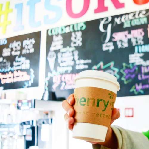 A person holds a coffee cup in front of a colorful menu board with various food and drink options.