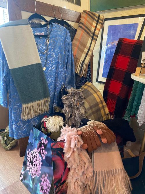 A display of various clothing items and scarves in different colors and patterns, arranged on hangers and a table.