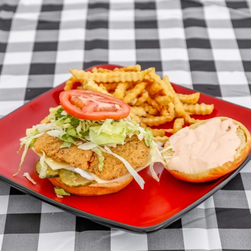 A crispy chicken sandwich topped with lettuce and tomato, served with crinkle-cut fries on a checkered tablecloth.
