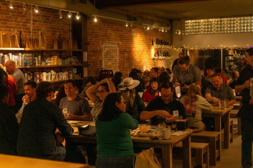 A lively café with people socializing, playing games, and enjoying food in a cozy, brick-walled setting.