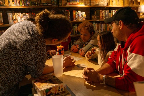 A group of four people gathered around a table, focused on a game with colorful pieces and cards in a cozy setting.