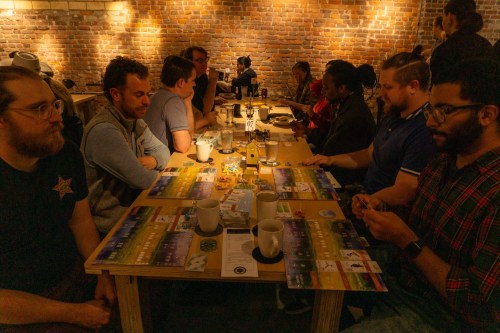 A group of people seated at a table playing board games in a cozy, brick-walled café setting.