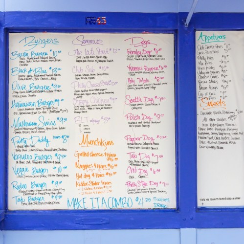 Menu board featuring burgers, sandwiches, hot dogs, appetizers, and desserts with prices listed.