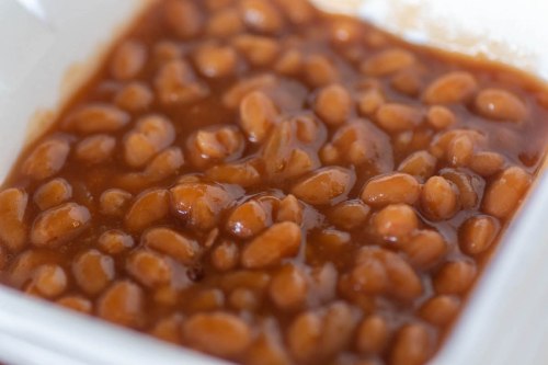 A close-up of baked beans in a rich, brown sauce served in a white bowl.