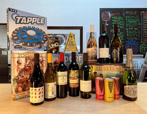 A collection of board games and various wine bottles arranged on a table, with colorful cans in the foreground.