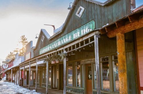 A rustic wooden storefront with a sign reading "Palmer's Exchange" in a snowy, sunlit setting.