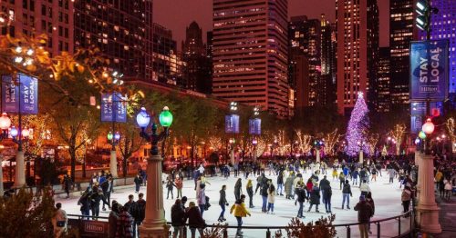 A bustling ice skating rink surrounded by city skyscrapers, illuminated by colorful lights and a festive tree at night.