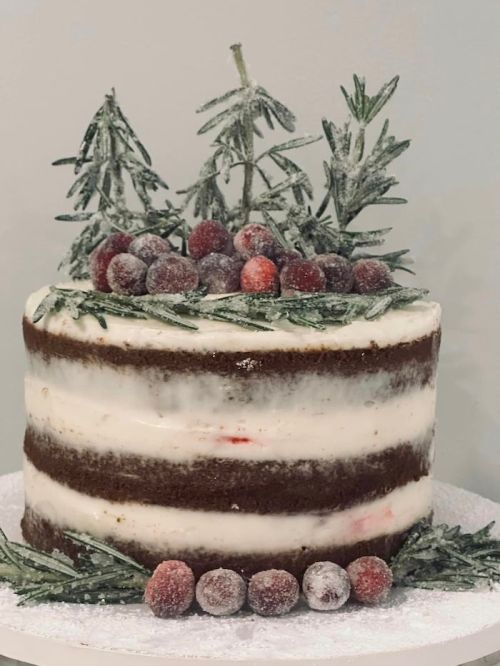 A layered cake decorated with frosted berries and rosemary, resembling a winter scene.