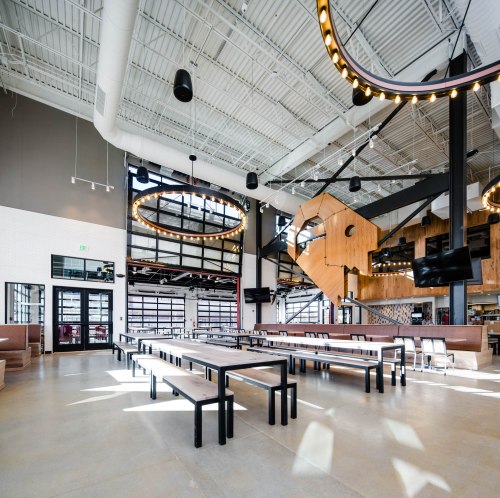 Modern restaurant interior featuring long wooden tables, large circular light fixtures, and an open, airy design.
