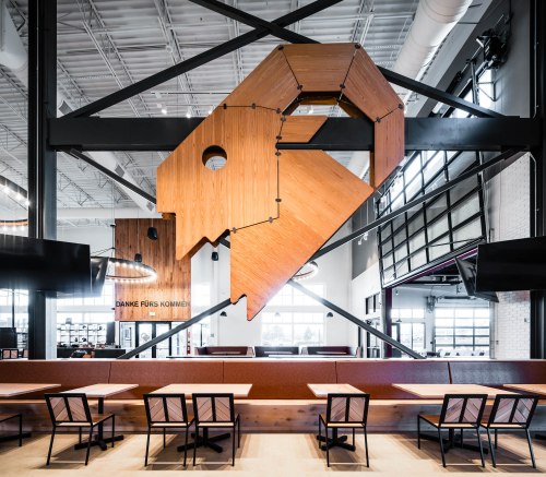 Modern restaurant interior featuring a large wooden fish sculpture and minimalist seating arrangements.