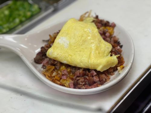 A plate of hash browns topped with diced ham and a fluffy yellow omelet.