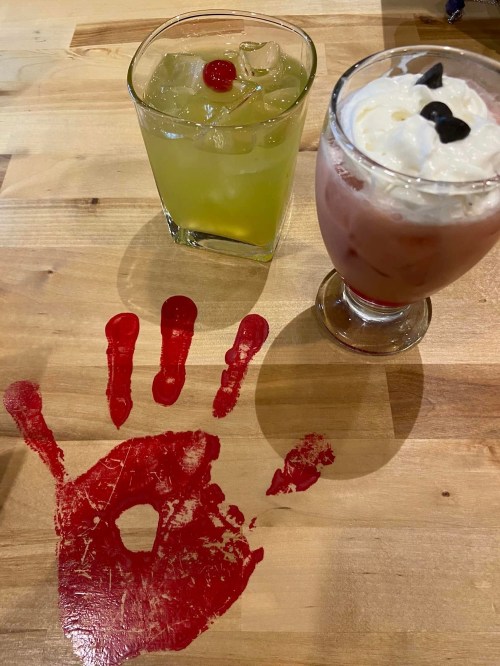 Two colorful drinks on a wooden table, with a red handprint painted beneath them.