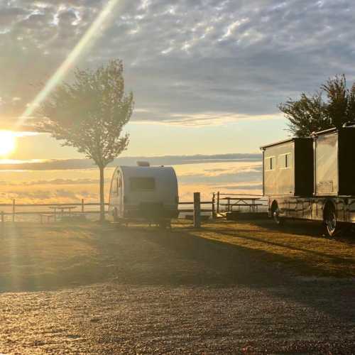 A serene sunset over a grassy area with a small camper and a larger trailer parked nearby.