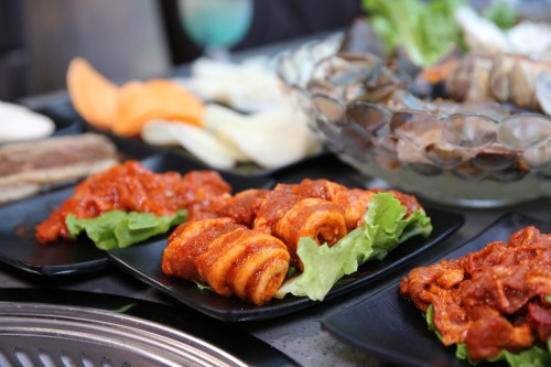 Plates of marinated meat on lettuce, with a variety of seafood and vegetables in the background.