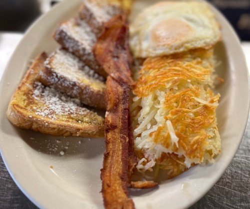 A plate of breakfast featuring French toast, crispy bacon, a fried egg, and golden hash browns.