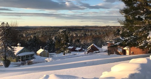 A snowy landscape with colorful houses and trees, under a clear sky with soft clouds.