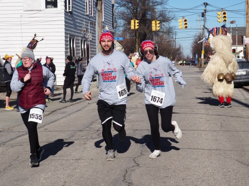 Three runners in matching shirts participate in a fun run, with a costumed figure in the background.