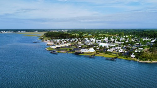 Aerial view of a coastal area with a marina, green land, and a small community along the water's edge.