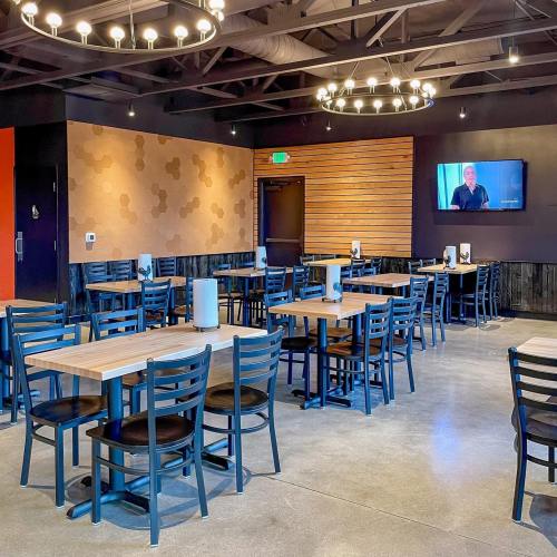 Modern restaurant interior with wooden tables, black chairs, and a TV on the wall. Soft lighting and a cozy atmosphere.