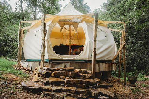 A cozy yurt nestled in a forest, featuring a wooden deck and stone steps leading to its entrance.