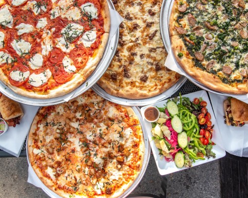 A variety of pizzas with different toppings, alongside a fresh salad with assorted vegetables.