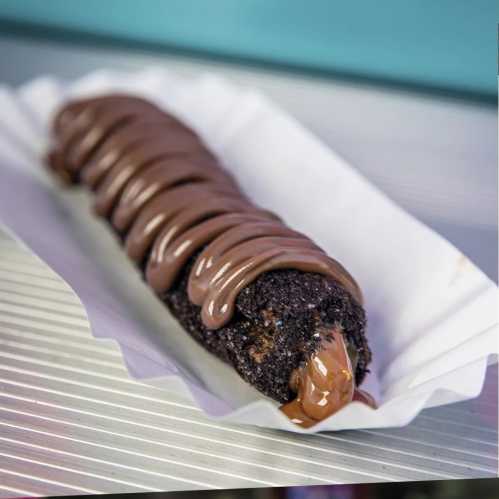 A chocolate-covered dessert with a rich, dark exterior and a glossy chocolate drizzle on top, served in a paper tray.