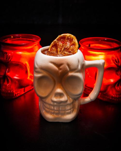 A skull-shaped mug filled with a drink, surrounded by glowing red skull-shaped glasses.