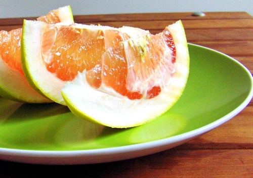 Sliced grapefruit on a green plate, showcasing juicy pink segments against a wooden background.