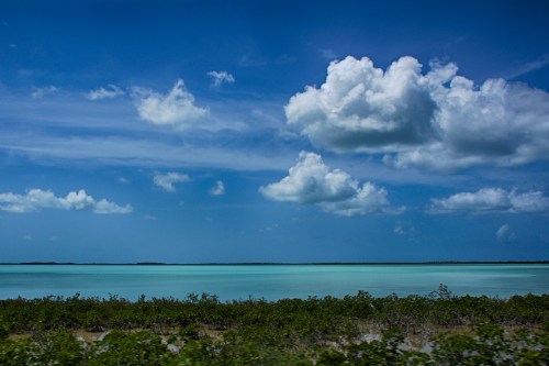 A serene coastal landscape featuring turquoise waters, lush greenery, and fluffy clouds under a bright blue sky.