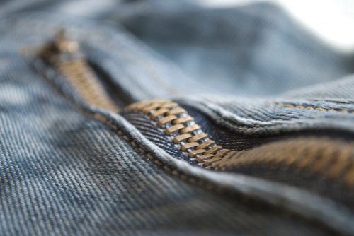 Close-up of a denim fabric with a partially unzipped zipper, showcasing the stitching and metal teeth.