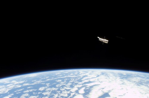 The Hubble Space Telescope orbits above Earth, with a view of the planet's clouds and curvature against a black sky.