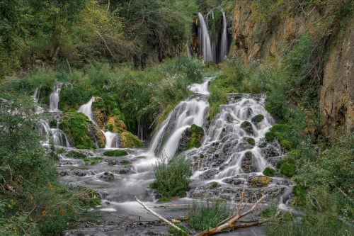 A serene waterfall cascades over moss-covered rocks, surrounded by lush greenery and flowing streams.