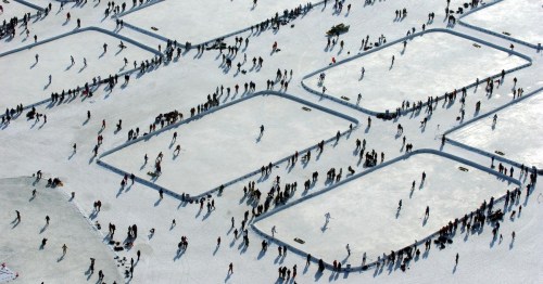 Aerial view of a frozen lake with numerous people skating and enjoying winter activities on the ice.