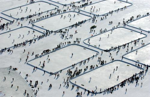 Aerial view of a frozen rink with numerous people skating in designated rectangular areas.
