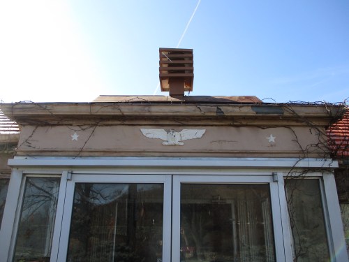 A building facade featuring an eagle emblem, stars, and a chimney against a clear blue sky.