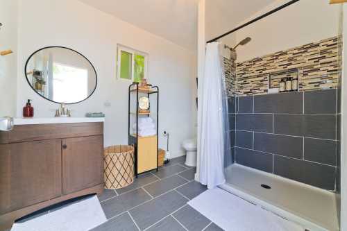 Modern bathroom featuring a shower, vanity with sink, and storage cart, with neutral tones and stylish decor.