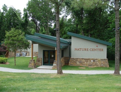 A modern nature center building with a stone base, surrounded by trees and greenery. Sign reads "NATURE CENTER."