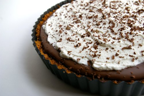 A chocolate cream pie with a graham cracker crust, topped with whipped cream and chocolate shavings.