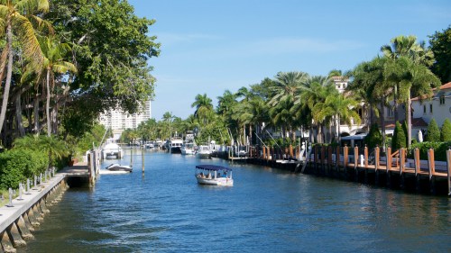A serene canal lined with palm trees and boats, under a clear blue sky.
