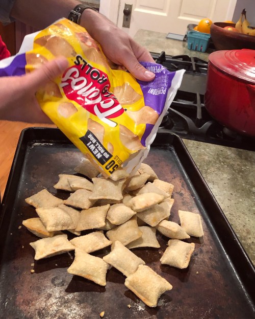 A person pours a bag of Tostitos rolls onto a baking tray in a kitchen.